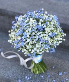 a bouquet of blue and white flowers on the ground with a ribbon tied around it