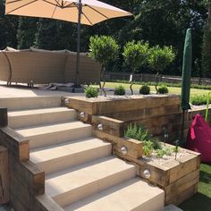 an outdoor patio area with steps, planters and umbrellas on the grass in front of it