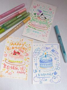 four birthday cards with markers and pencils next to one that has a cake on it