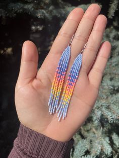 a hand holding two pairs of multicolored beaded earrings on it's palm