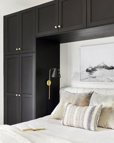 a bedroom with black cabinets, white bedding and a gold accent light on the wall