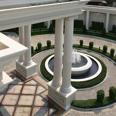 an aerial view of a fountain surrounded by white pillars and trimmed with greenery in the center