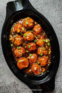 meatballs with sauce and green onions in a black crock pot on a table