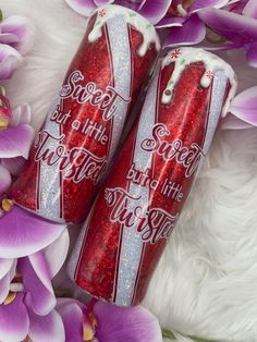 two coca - cola cans sitting next to each other on top of purple orchids