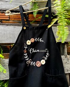 a black apron with buttons hanging from it's side on a clothes line next to some plants