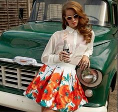 a woman standing in front of a green truck holding a bottle and posing for the camera