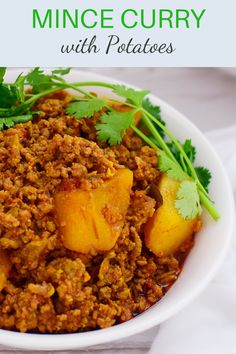 a white bowl filled with potatoes and meat next to cilantro on top of a table