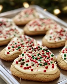 cookies with white frosting and sprinkles are on a tray near a christmas tree