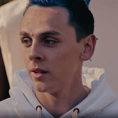 a young man with blue hair wearing a white hoodie and looking at the camera