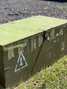 an old wooden box with graffiti on it sitting in the grass next to a street