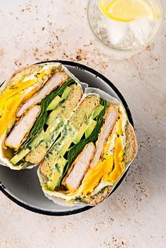 two sandwiches with meat, cheese and spinach are on a plate next to a glass of water