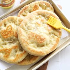 three biscuits in a baking pan with a yellow spatula on the side and a bottle of honey nearby