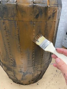 a person holding a paintbrush in front of a wooden barrel