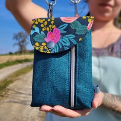 a woman holding a blue purse with flowers on it and a chain hanging from the front