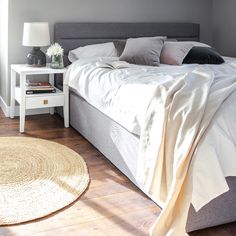 a bed sitting in a bedroom next to a white table with a lamp on it