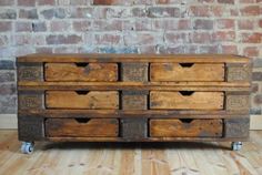 an old wooden dresser sitting on wheels in front of a brick wall and hardwood floor