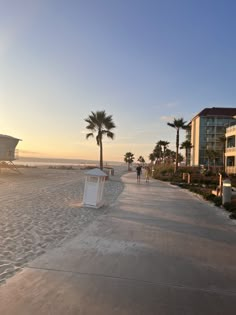 people walking on the beach at sunset with palm trees and buildings in the background as the sun sets