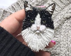 a black and white cat brooch sitting on top of a knitted blanket next to someone's hand