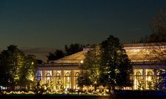 a building lit up at night with trees and lights on the front, reflecting in water