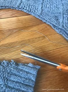 a pair of scissors and some knitting needles on a table next to a blue sweater