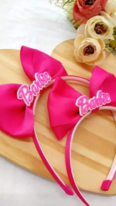 two pink bow headbands with the word barbie on them sitting on a wooden board