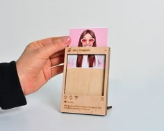 a hand holding a wooden photo frame with a woman's face on the front