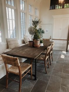 a dining room table with chairs and potted plants on it in front of two windows