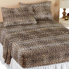 a bed with a leopard print comforter and two pillows on top of it next to a night stand