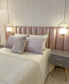 a bed with two lamps hanging above it and some pillows on top of the bed