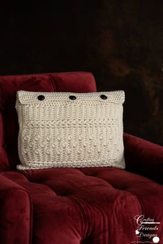 a red chair with a white knitted pillow on it's back in front of a dark wall