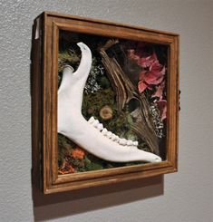 there is a fake white shoe on display in a wooden frame with flowers around it