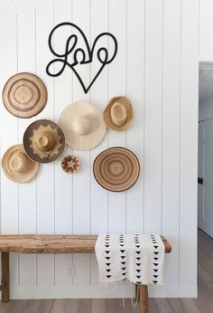 a wooden bench sitting next to a wall with hats hanging on it's side