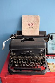 an old fashioned black typewriter sitting on top of a red table next to books