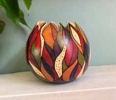 a colorful vase sitting on top of a table next to a green leafy plant