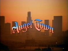 the logo for angel town in front of a cityscape with skyscrapers at sunset