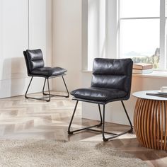 two black leather chairs sitting in front of a round table on top of a hard wood floor