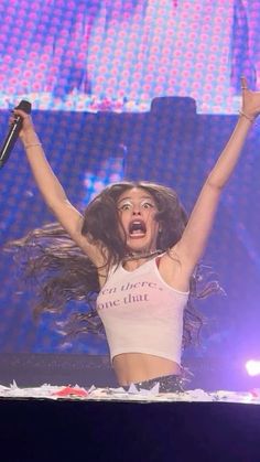 a woman with her arms in the air while holding a microphone and singing on stage