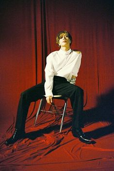 a man sitting on top of a chair in front of a red curtain with his eyes closed