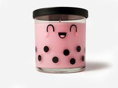 a pink candle with black polka dots and a smiling face on the front, sitting against a white background