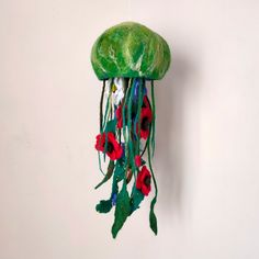 a green jellyfish with red flowers hanging from it's side on a white wall