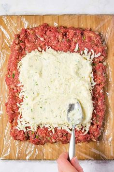 someone using a spoon to spread cheese on top of ground meat in a square pan