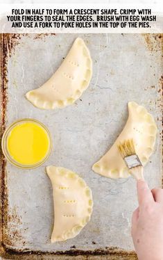 someone using a paint brush to make empanadas on a baking sheet with text overlay