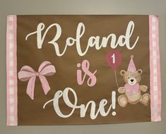 a brown and pink wall hanging with a teddy bear holding a balloon, the words roland is one on it