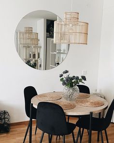 a dining room table with black chairs and a round mirror