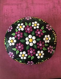 a painted rock sitting on top of a pink table next to a red wall with white and yellow flowers