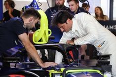 two men working on a race car in a garage with other people looking at it