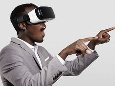 a man in a suit pointing at something with a virtual headset on his head