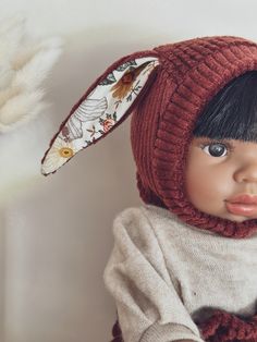 a doll wearing a red knitted hat and scarf next to a white feathered object