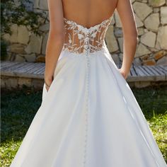 the back of a woman's wedding dress in front of a stone wall and grass