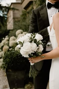 a bride and groom standing next to each other in front of some bushes with white flowers